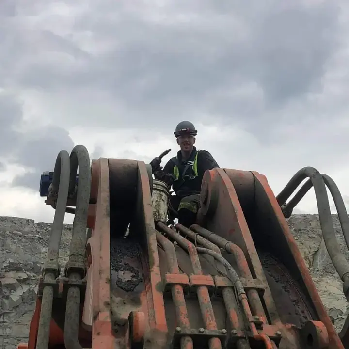 Jarrad in a hard hat and harness, on top of a machine at a mine